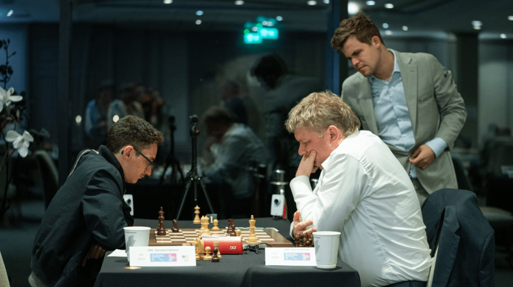 Caruana (left) playing Shirov (right) while Carlsen (standing) observes at the 2019 FIDE Chess.com Grand Swiss. Photo: Maria Emelianova/Chess.com.